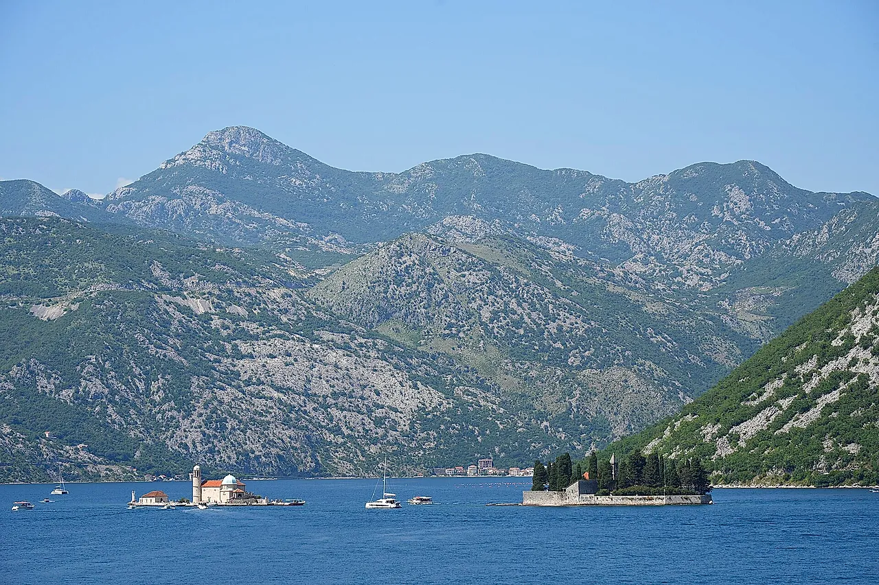 Die Bucht von Kotor bei Perast, mit den zwei Inseln in der Ferne und Bergen unter blauem Himmel
