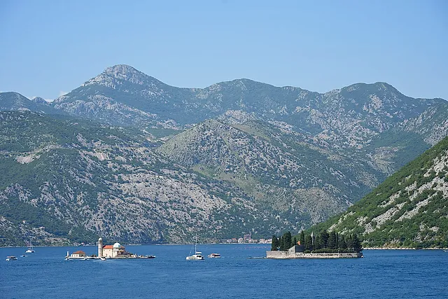 Die Bucht von Kotor bei Perast, mit den zwei Inseln in der Ferne und Bergen unter blauem Himmel
