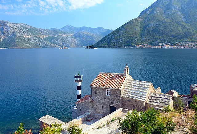 Die Bucht von Kotor von der Straße bei Lepetane: eine kleine Steinkirche mit gestreiftem Leuchtturm, Perast in der Ferne und Berge