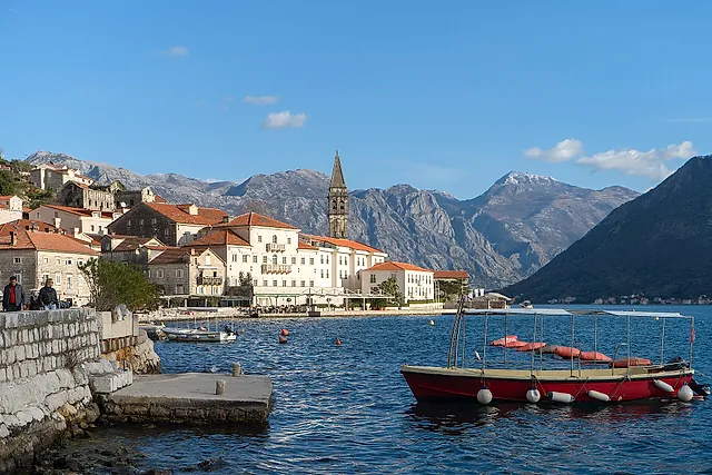 Perast with its bell tower, a red boat and the mountains behind