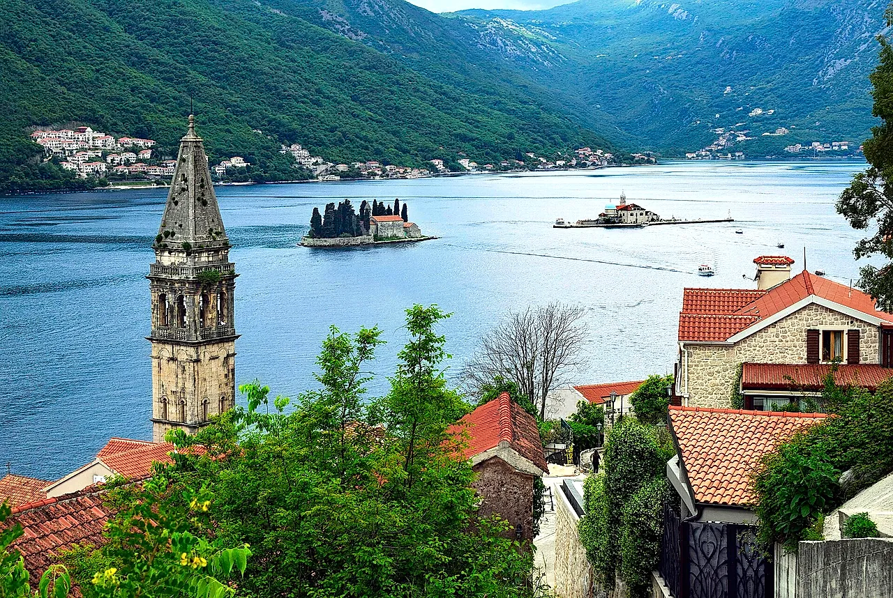 View from above Perast: a bell tower in the foreground, red roofs, the two islets in the bay and the mountains