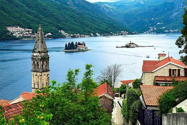 View from above Perast: a bell tower in the foreground, red roofs, the two islets in the bay and the mountains