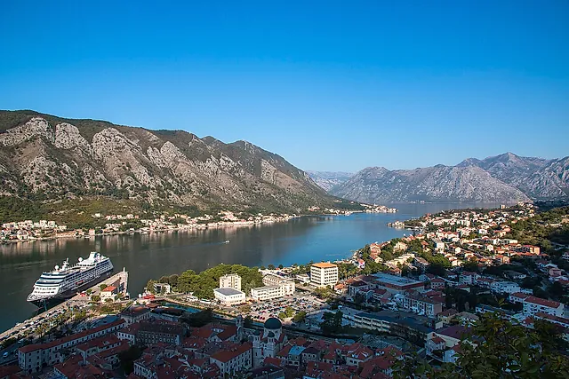 A cruise ship moored at the quay in the Bay of Kotor, seen from above, with the roofs of the old town below
