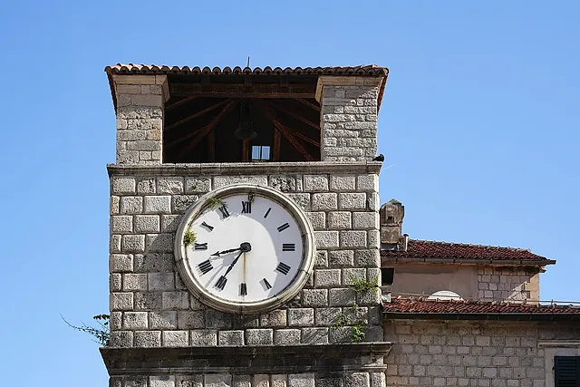 The clock tower of Kotor, a stone tower with a white clock face against a blue sky